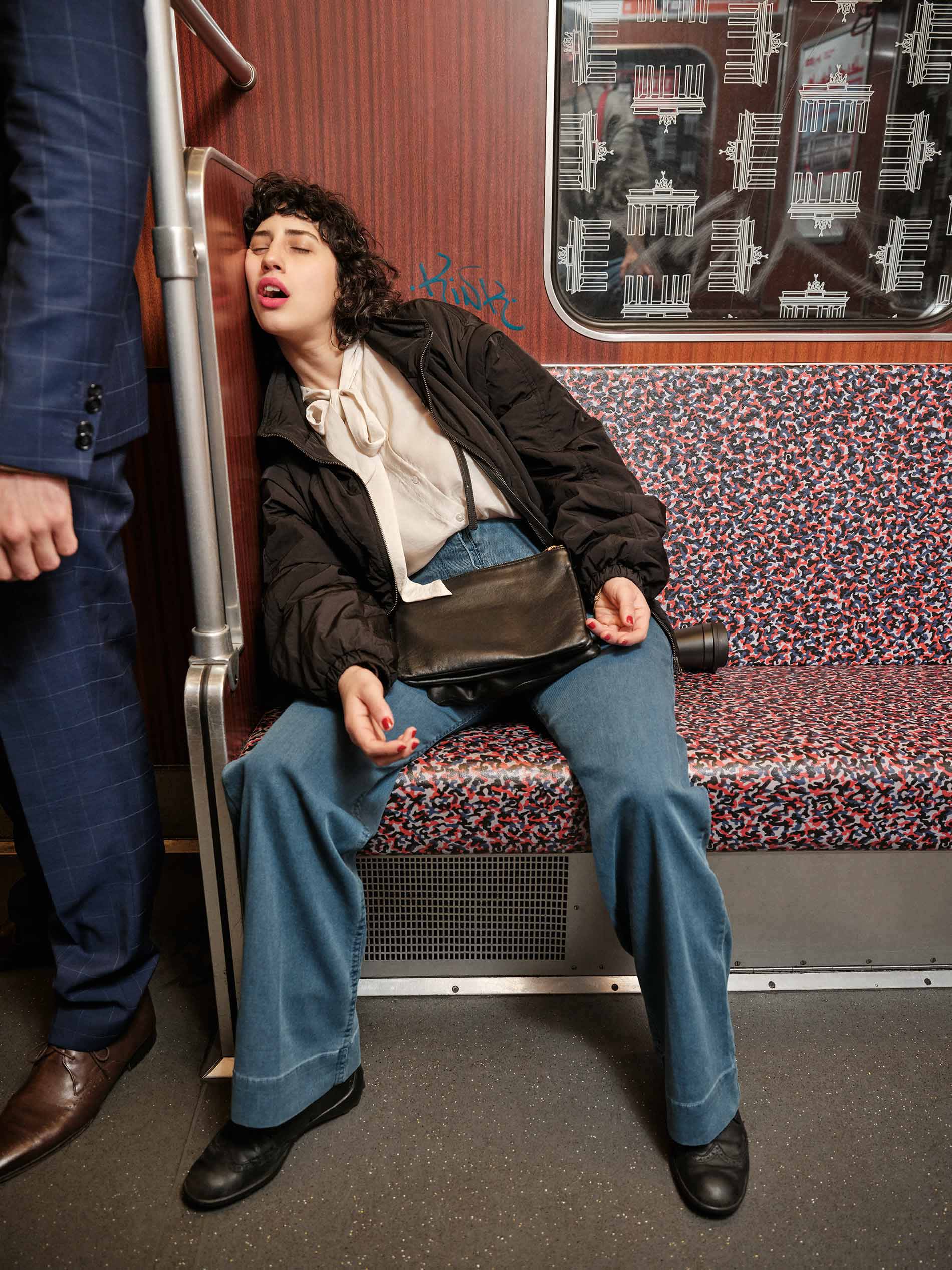 Een jonge vrouw slaapt met geopende mond geleund tegen een muurtje en met schoudertas in de Berlijnse metro | mey®