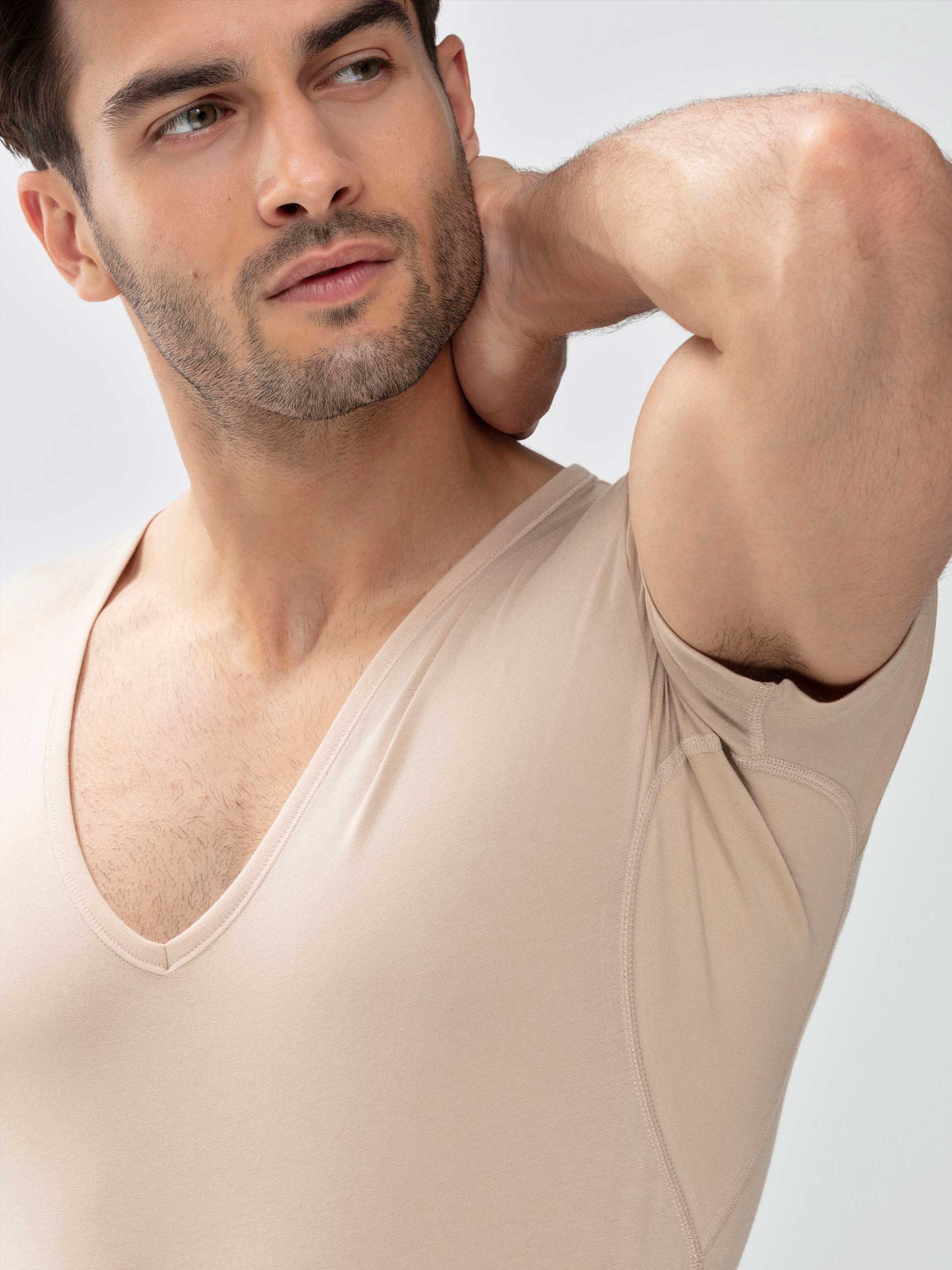 Man wears the undershirt in the colour Light Skin; his arm is angled upwards and the inserts with silver ions are visible under the arms. | mey®