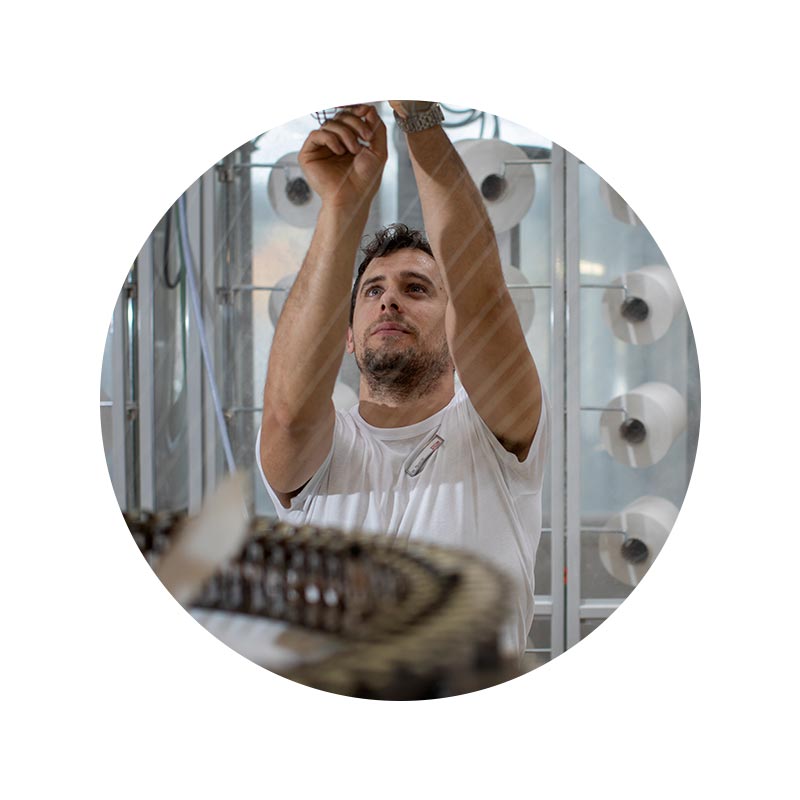 Mitarbeiter Portrait von Danijel Kucic an einer Strickmaschine, an der etwas repariert werden muss | mey® 