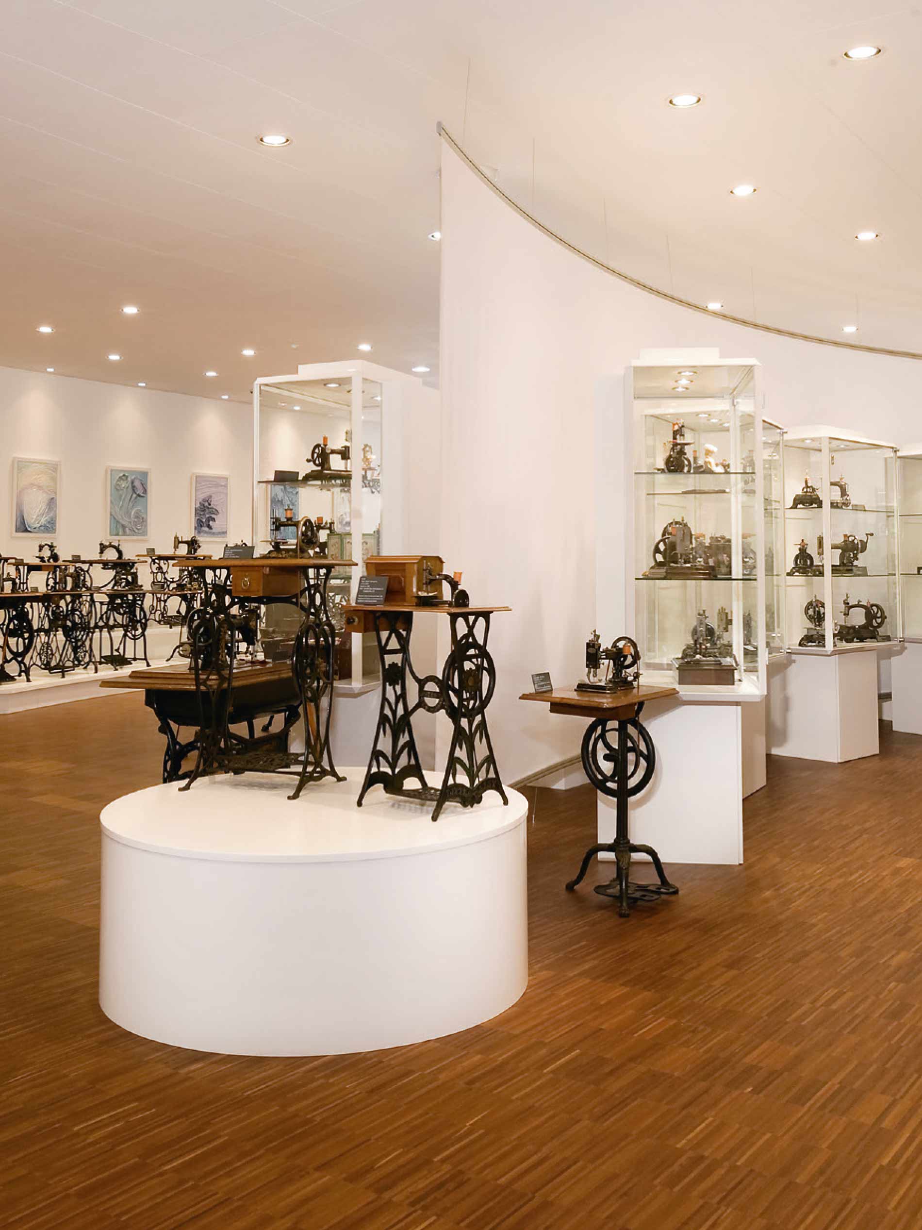 Interior view of the sewing machine museum with small sewing machines on a pedestal and display cases in the background | mey®