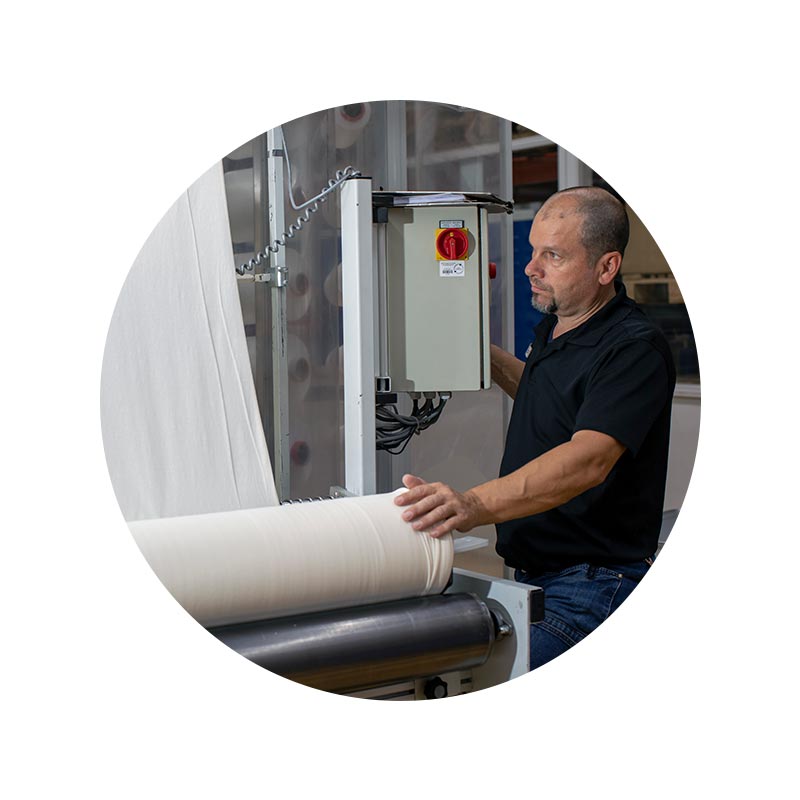 Employee portrait of Jürgen Grom in front of a roll of fabric for quality control in the knitting department  | mey®