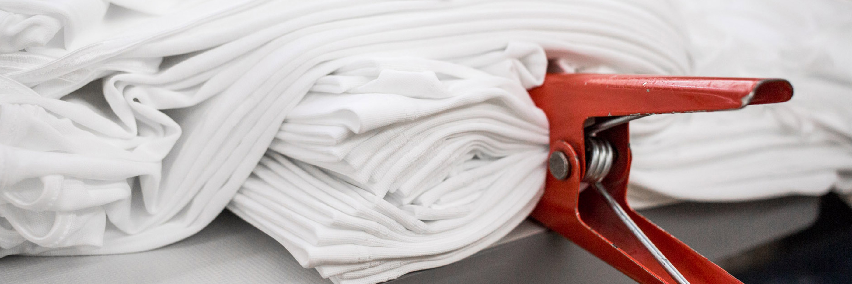 Witte stof, in meerdere lagen geplooid en met een rode klem vastgemaakt, voorbereiding voor het kalanderproces | mey®