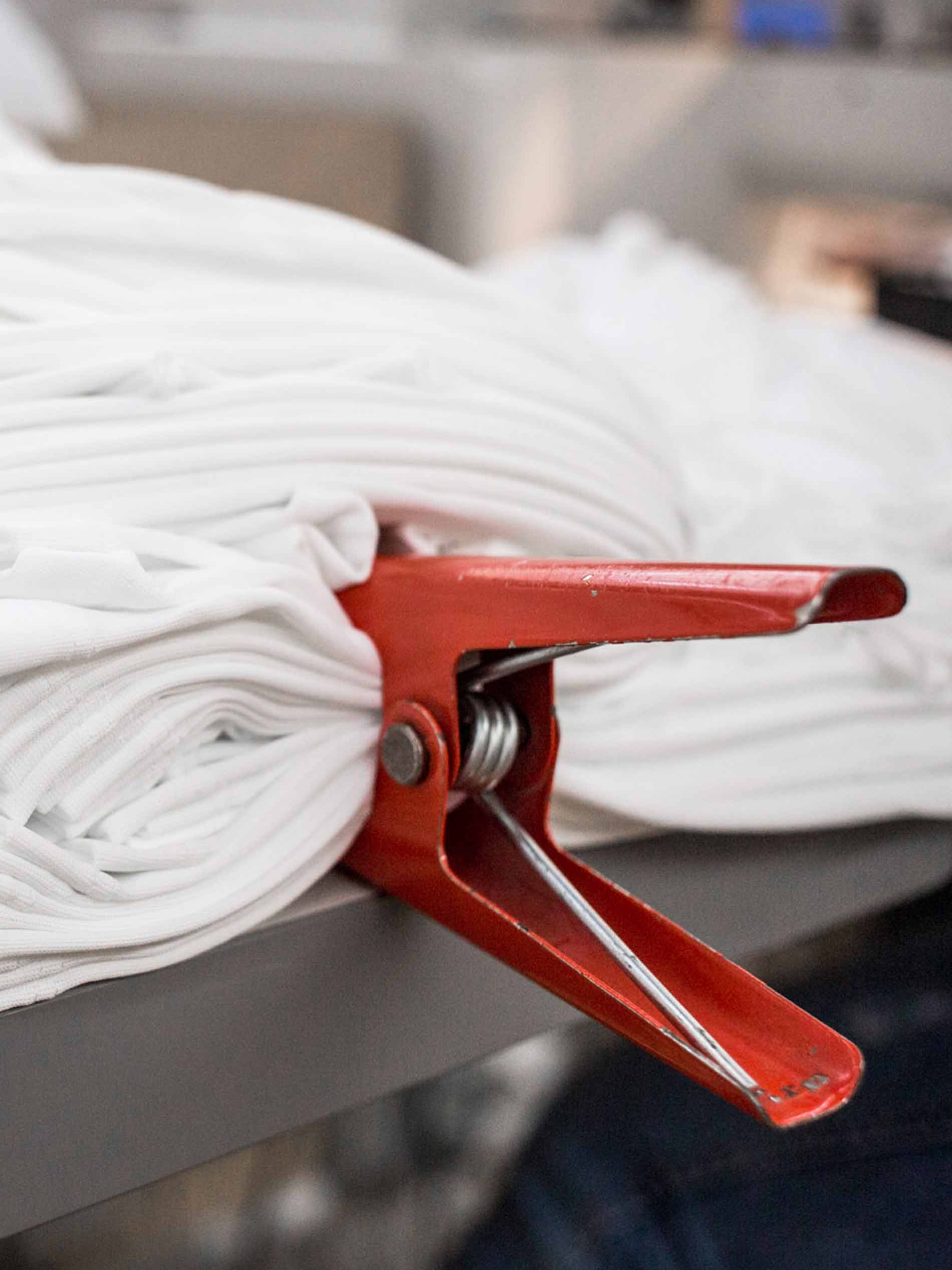 White fabric, folded into multiple layers and fixed in place with a red clip, preparation for the calendering process | mey®
